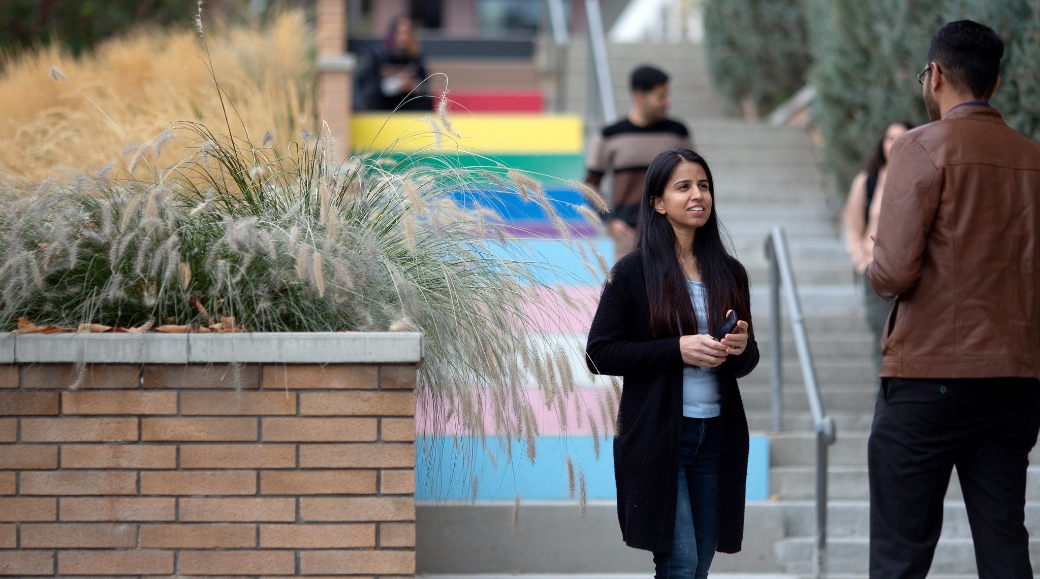 Two students stand in front of the rainbow stairs in front of the UNC. They are chatting happily.