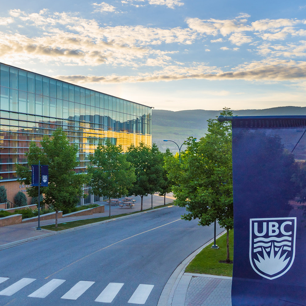 An aerial shot of University Way, looking east. The UNC building is to the left. A blue flag with the UBC emblem is visible in the foreground.