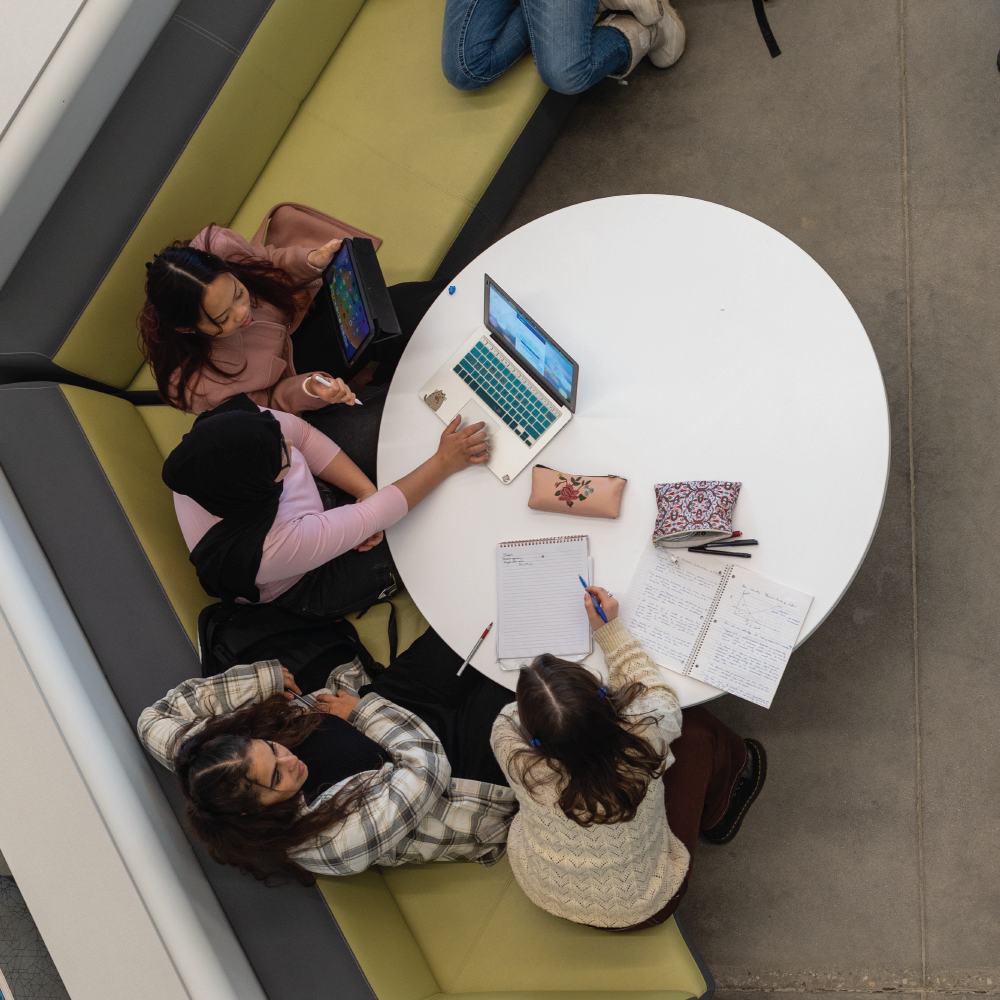 Students-studying-in-the-UBCO-Commons-building.-They-are-stitting-around-a-table-and-sharing-notes