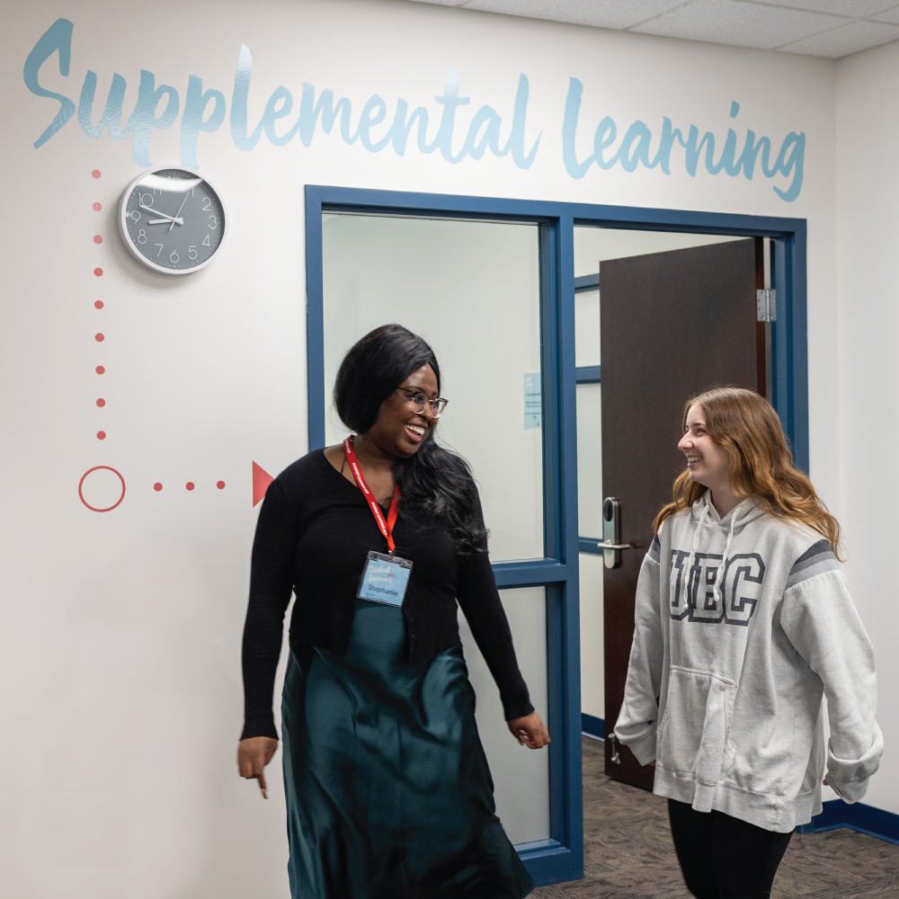 Two students walking out of the Supplemental Learning room at UBC Okanagan's Student Learning Hub. They are looking at each other and smiling