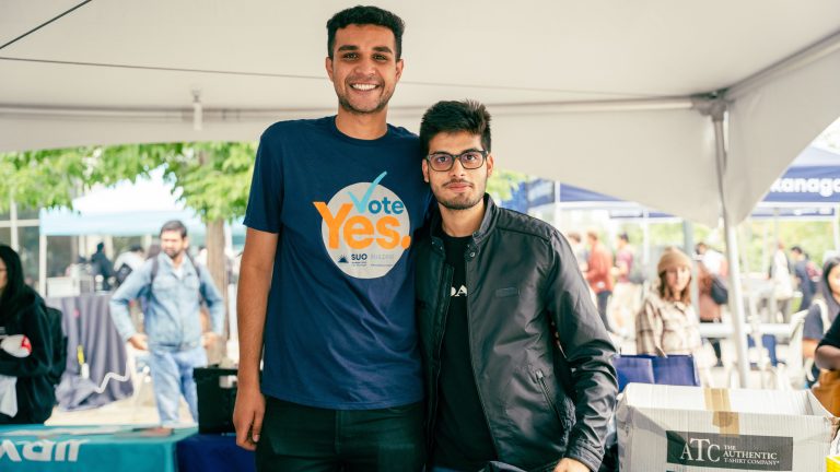 Two men at an event. One is wearing a Yes Vote shirt