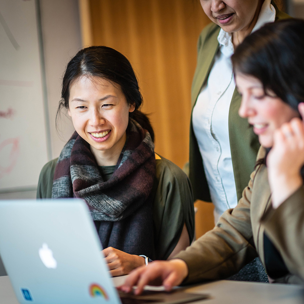 A smiling student sits next to a staff member, both looking at a laptop screen.