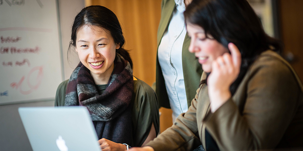 A smiling student sits next to a staff member, both looking at a laptop screen.