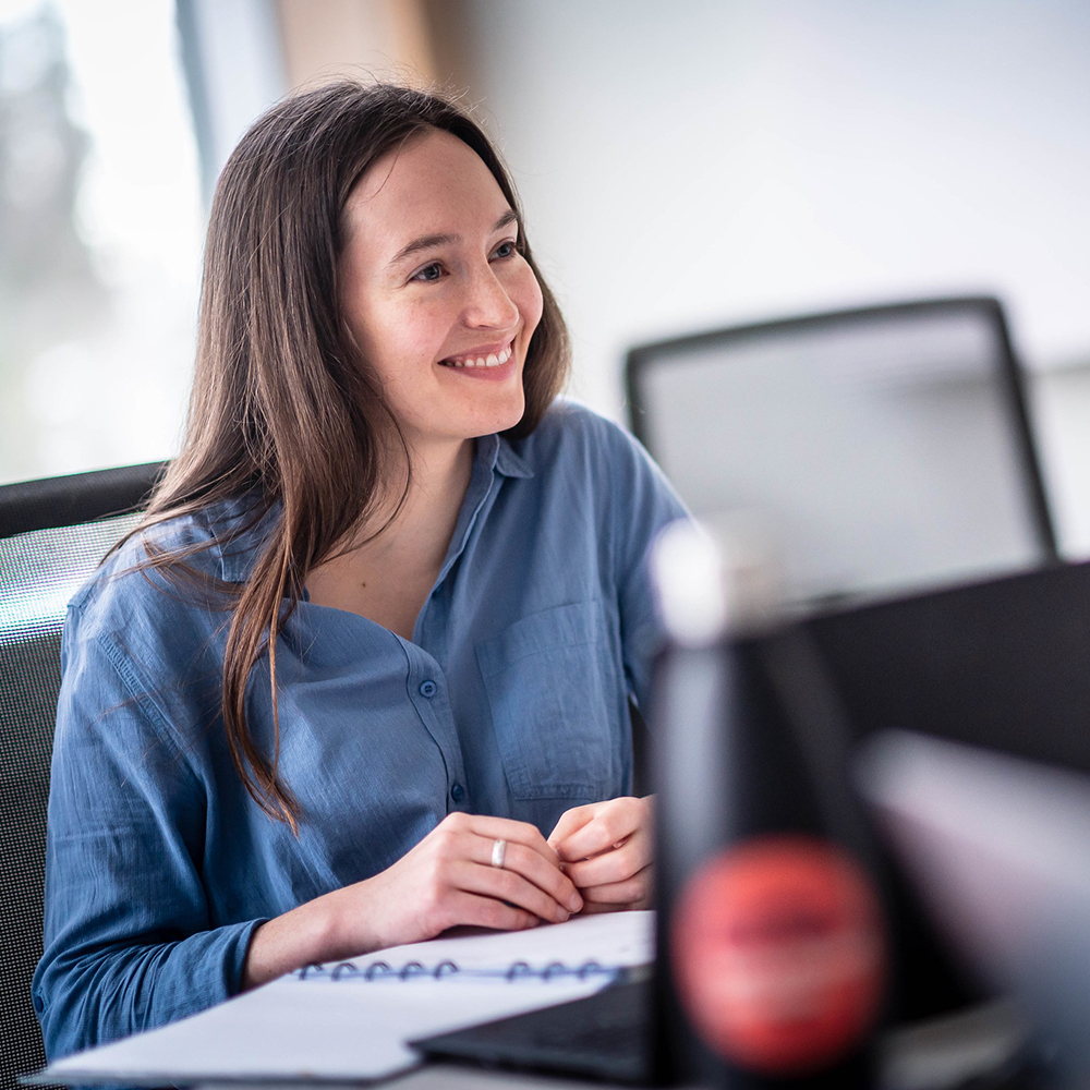 A female student looks up from her laptop, smiling at someone out of frame.