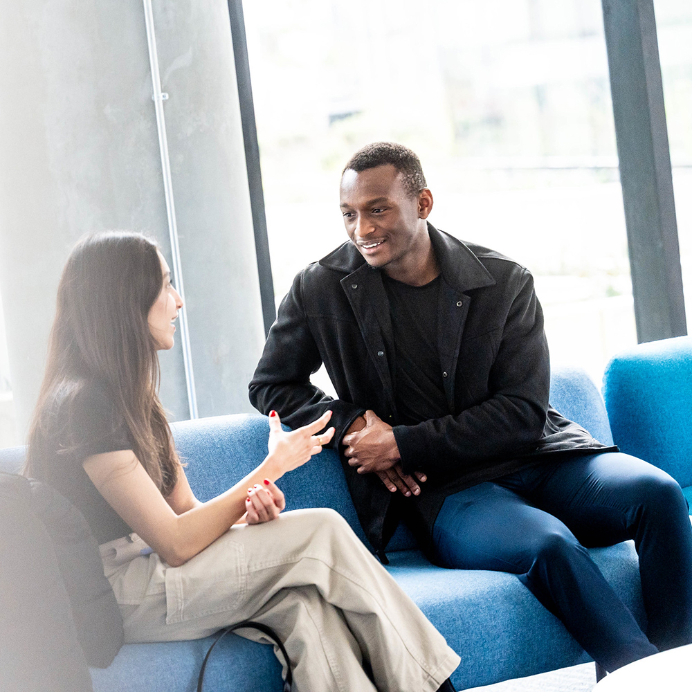 A man and woman sitting on a blue sofa, engaged in conversation