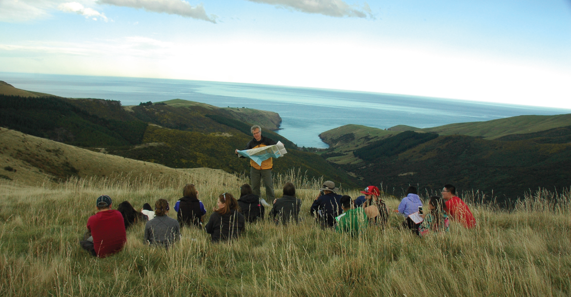 Students sitting in tall grass for their lecture while looking over the ocean during their Global Seminar experience.