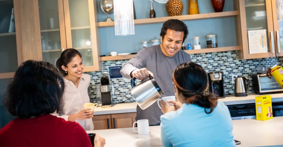 four students enjoying tea in a Collegia kitchen space. one student is pouring hot water from the kettle for the other students